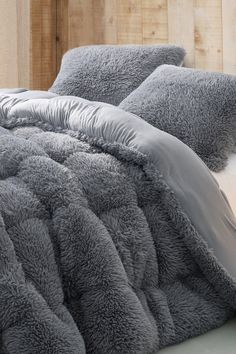 a bed covered in grey fluffy blankets and pillows