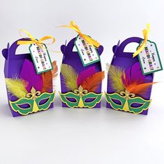 three purple boxes with masks on them and tags attached to the top, one is for mardi gras