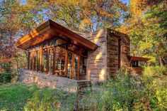 a small cabin in the woods surrounded by trees and grass with fall foliage around it