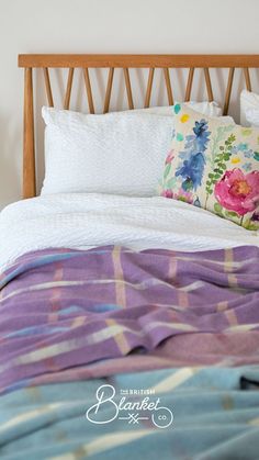 a bed with colorful blankets and pillows on it's headboard, in front of a white wall