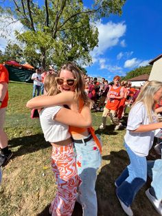 two women hugging each other in the middle of a group of people standing on grass