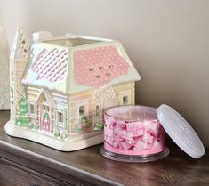 a pink candle sits on top of a wooden table next to a house shaped container