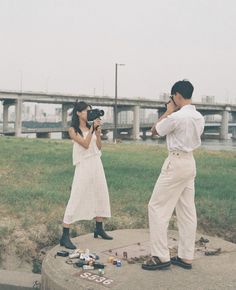 a man and woman taking pictures in front of a bridge with a camera on the ground