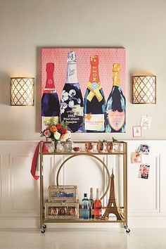 a bar cart with wine bottles on it in front of a wall mounted art piece