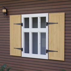 a window with wooden shutters on the side of a brown wall next to a potted plant