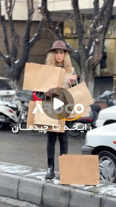 a woman is standing on the sidewalk with boxes in front of her and holding bags behind her