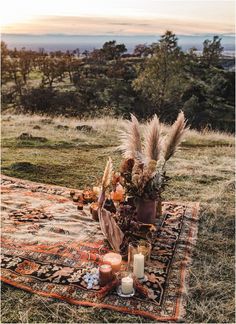 a rug with candles and flowers on it in the middle of an open field near some trees