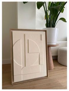 a plant is sitting next to a white framed painting on the floor in front of a potted plant