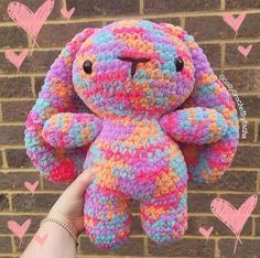 a crocheted teddy bear is held up in front of a brick wall with hearts