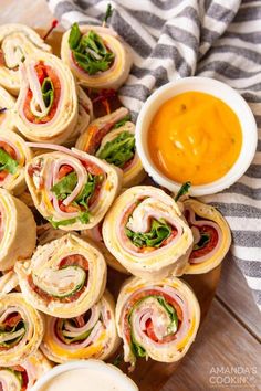 a platter filled with sandwiches and dipping sauces on top of a wooden table