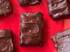 brownies with chocolate frosting sitting on a red surface, ready to be eaten