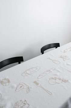 a white table with black chairs in front of it and drawings on the tablecloth