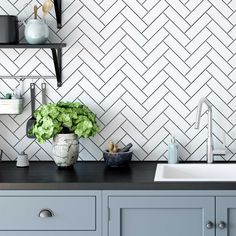 a kitchen with white and black tiles on the wall, green plants in a vase