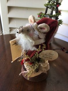 a stuffed mouse in a santa hat with a sign on it's chest sitting on a table