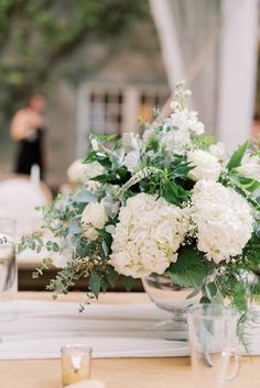 a vase filled with white flowers sitting on top of a table next to glasses and candles