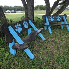 two wooden benches with paw prints painted on them sitting in the grass under a tree