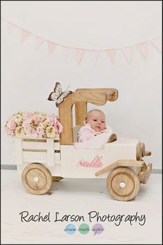 a baby is sitting in a toy truck with flowers on the bed and bunting