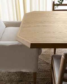 a wooden table sitting in front of a white chair next to a plant on top of a rug