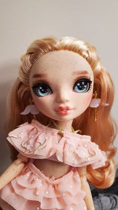 a close up of a doll with blonde hair and blue eyes wearing a pink dress