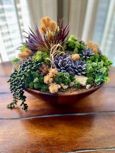 an arrangement of succulents and plants in a bowl on a wooden table