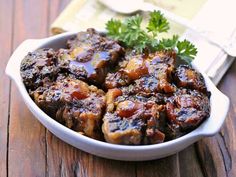 a white bowl filled with meat covered in sauce and garnished with parsley