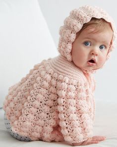 a baby wearing a pink crochet sweater and bonnet