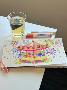 a cup of tea, pencils and an open notebook on a table with a carousel theme