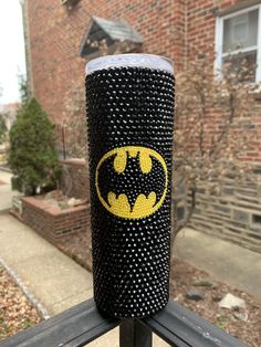 a black and yellow cup with a batman symbol on it sitting on a fence post