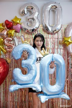 a woman standing in front of balloons that spell out the number 30 and holding up her hand