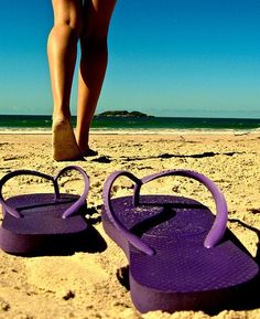 pair of purple flip flops on sandy beach with blue sky and ocean in background