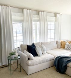 a living room with white couches and pillows on the floor next to two windows