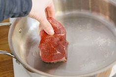 a piece of meat is being cooked in a saucepan on a stove top with a person's hand reaching for it