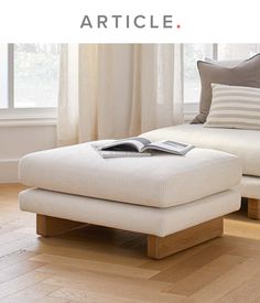 a white ottoman sitting on top of a hard wood floor next to a window with curtains