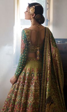 a woman in a green and gold lehenga with her back to the camera