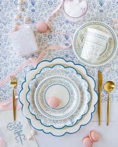 a table set with plates, silverware and pink macaroons