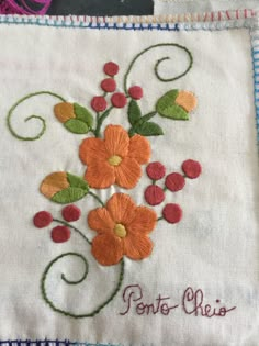 embroidered flowers on white fabric with red, orange and green leaves in the center that says pontot ches