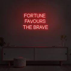 a red neon sign that says fortune favors the brave in front of a white cabinet