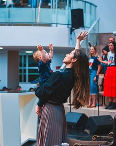 a woman holding a baby up in the air with other people standing around her watching