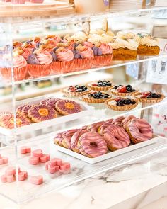 an assortment of pastries and desserts on display in a bakery case with pink icing