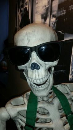 a fake skeleton wearing sunglasses and a green ribbon around it's neck is shown