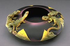 two lizards sitting on top of a black and yellow vase with gold trimmings