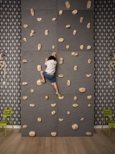 a man climbing up the side of a rock wall in a room with wood floors