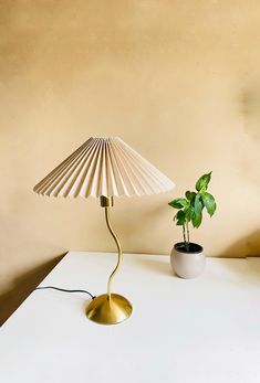 a white table with a gold lamp and a potted plant on the top shelf