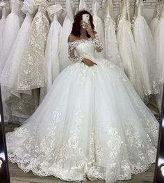 a woman taking a selfie in front of wedding gowns on display at a store