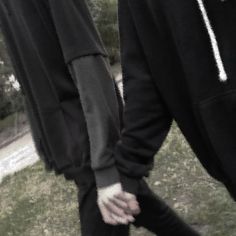 two people in black hoodies are holding hands with each other while walking through the grass