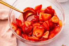 strawberries in a glass bowl being stirred with a spoon and placed on a white surface