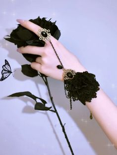 a woman's hand holding a black rose with chains and flowers attached to it