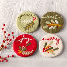 four embroidered christmas buttons sitting on top of a white cloth covered table next to red berries and twig