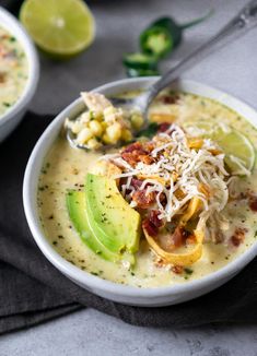 two bowls filled with soup and garnished with avocado, cheese and bacon