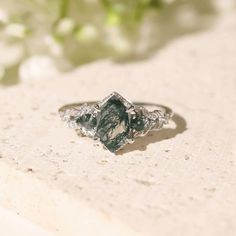 a close up of a diamond ring on a table with flowers in the back ground